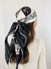 Side back view of a Classic woman wearing bespoke, luxury Elwyn New York silk scarf around her head . This geometric crazy quilt print is a vintage-modern depiction of the year 2020 filled with digital embroidery and lace of years past. One can see the word KIND depicted in this photo