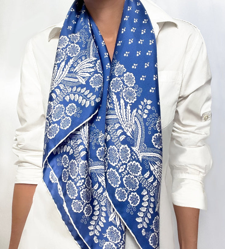 Woman wearing a bespoke Elwyn New York Scarf draped draped around her neck with an ornate, blue and white, vintage-pastoral bandana design. Classic, feminine, and romantic