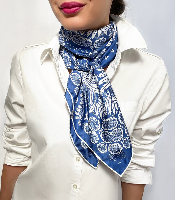 Woman wearing a personalized, bespoke Elwyn New York Scarf wrapped around her neck with an ornate, blue and white, vintage-pastoral bandana design. Classic, feminine, and romantic