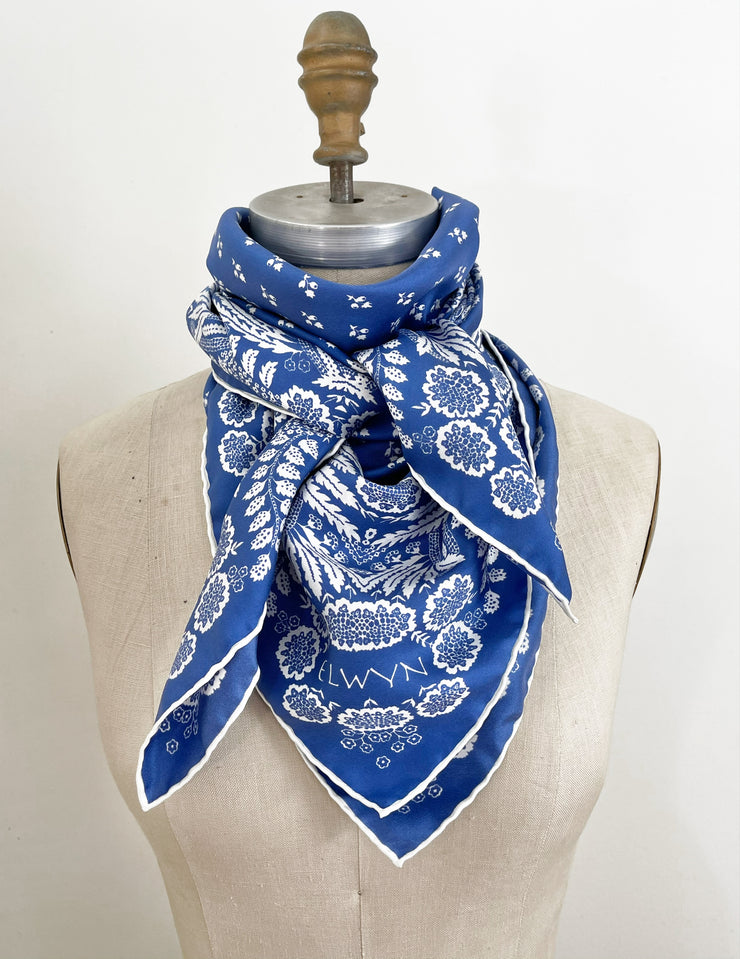 a bespoke Elwyn New York Scarf wrapped around the neck of a form with an ornate, blue and white, vintage-pastoral bandana design. Classic, feminine, and romantic