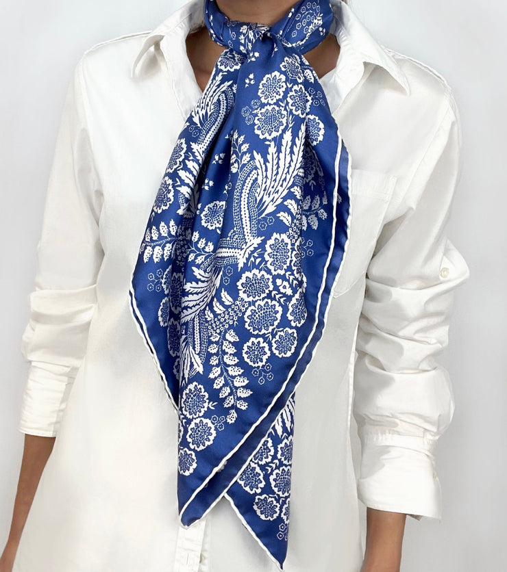 Woman wearing a personalized bespoke Elwyn New York Scarf draped knotted at the neck with an ornate, blue and white, vintage-pastoral bandana design. Classic, feminine, and romantic