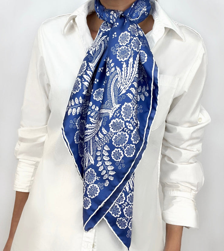 Woman wearing a bespoke Elwyn New York Scarf draped knotted at the neck with an ornate, blue and white, vintage-pastoral bandana design. Classic, feminine, and romantic