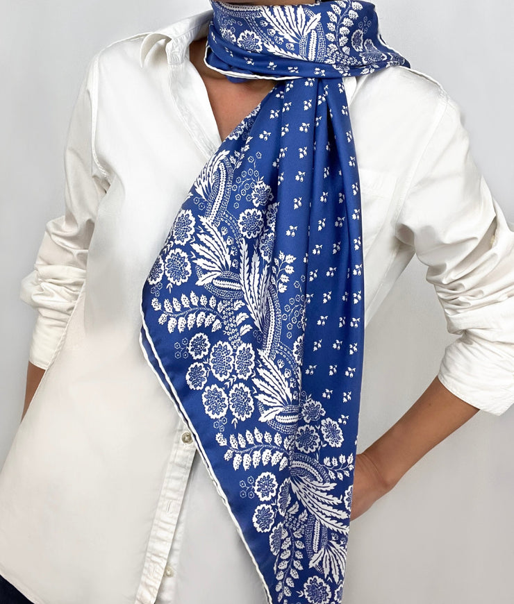Woman wearing a personalized bespoke Elwyn New York Scarf draped around her neck on one side with an ornate, blue and white, vintage-pastoral bandana design. Classic, feminine, and romantic