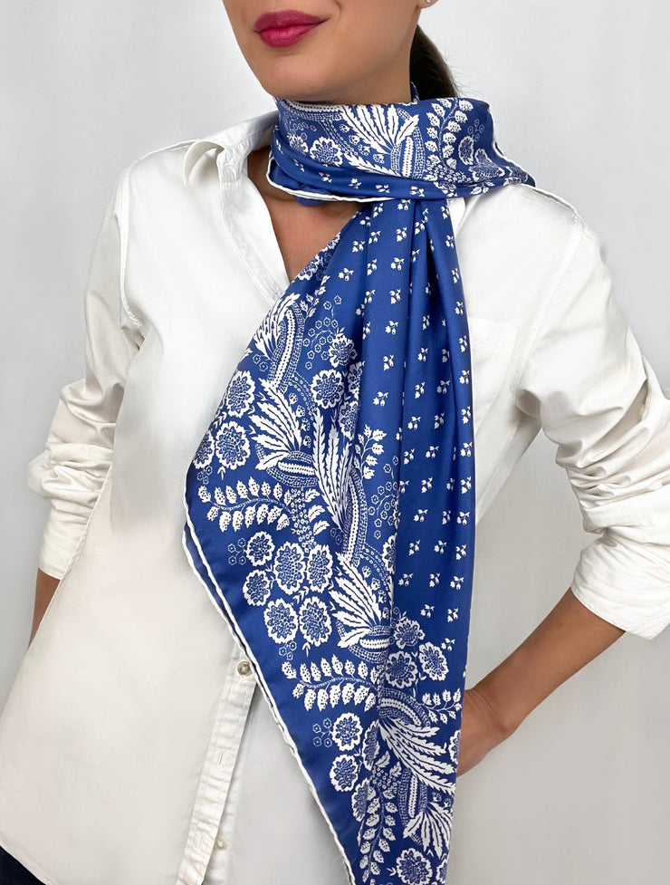Woman wearing a bespoke Elwyn New York Scarf draped around her neck on one side with an ornate, blue and white, vintage-pastoral bandana design. Classic, feminine, and romantic