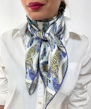 Woman wearing a bespoke Elwyn New York silk scarf around her neck, with a delightful design of swirling feathers, surrounded by creeping jaguars and parrots in the graphic border.