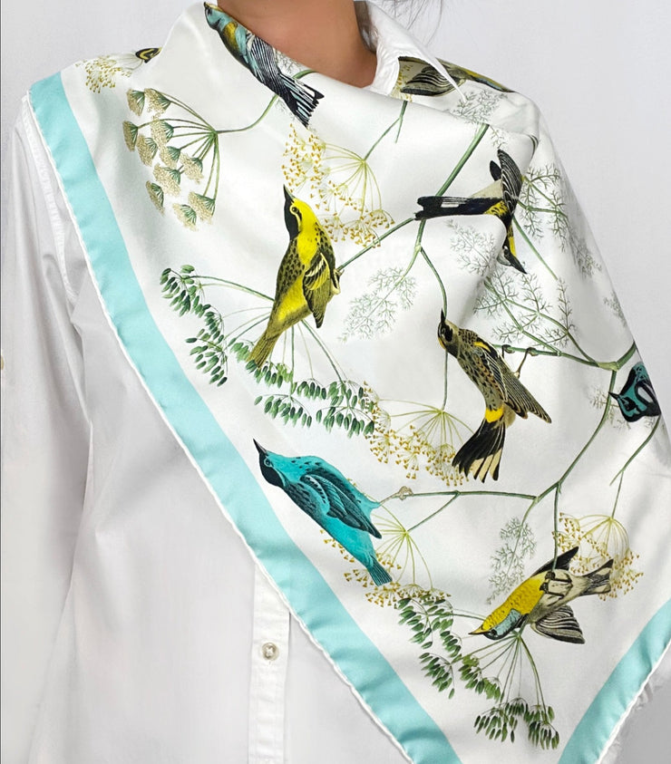 a classic woman wearing a bespoke Elwyn New York silk scarf draped around on her shoulders with a Charming blue and yellow warbler birds, flying and perched amidst delicate wild flowers. Inspired by nature found in the North East.