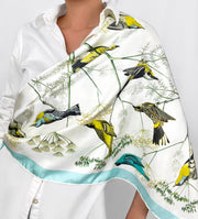 a classic woman wearing a personalized, bespoke Elwyn New York silk scarf draped around one shoulder with a Charming blue and yellow warbler birds, flying and perched amidst delicate wild flowers. Inspired by nature found in the North East.
