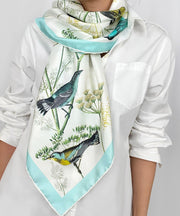 a classic woman wearing a bespoke Elwyn New York silk scarf draped around her neck on one side with a Charming blue and yellow warbler birds, flying and perched amidst delicate wild flowers. Inspired by nature found in the North East.
