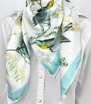 a classic woman wearing a bespoke Elwyn New York silk scarf around her neck with a Charming blue and yellow warbler birds, flying and perched amidst delicate wild flowers. Inspired by nature found in the North East.