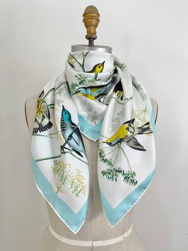 a bespoke Elwyn New York silk scarf around the neck of a form with a Charming blue and yellow warbler birds, flying and perched amidst delicate wild flowers. Inspired by nature found in the North East.